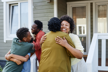 A group of people hugging outside a home.
